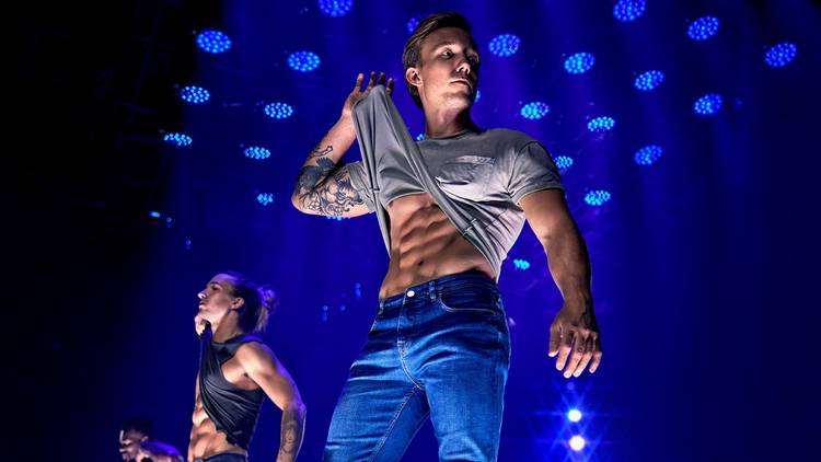 A Magic Mike Live dancer lifts his t-shirt to reveal rippling abs
