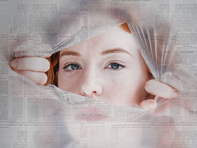 The Apologists, Old 505 Theatre 2021 A red-headed woman peering through a torn hole in a newspaper