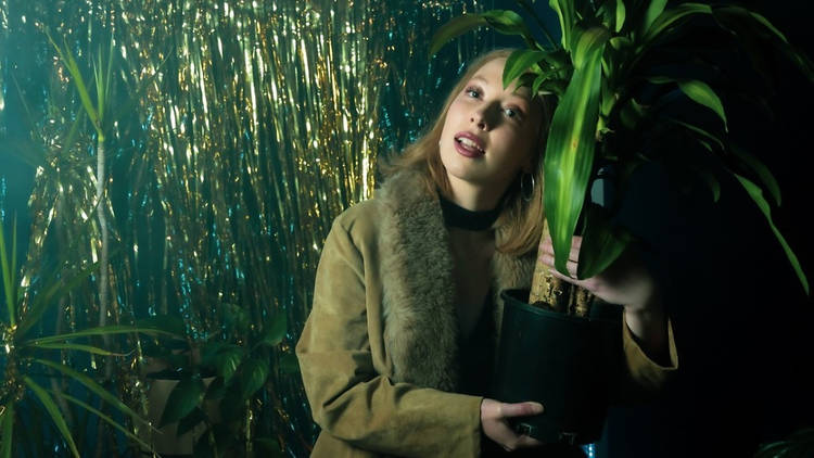 A woman wearing a fur-lined coat holds a pot plant close
