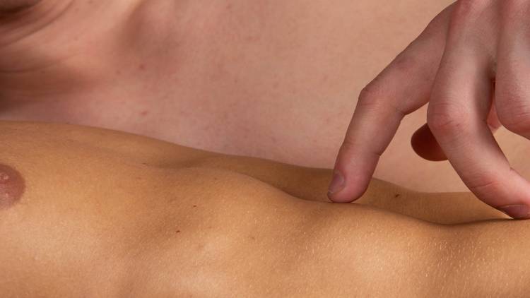 A close up of two naked male torsos, one man walks his fingers across the other's abs