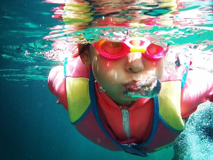 Child swimming in pool wearing goggles and vest