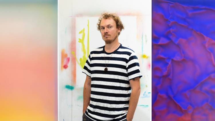 MUltimedia artist Daniel O’Toole, wearing a striped black and white t-shirt, framed by his colourful art