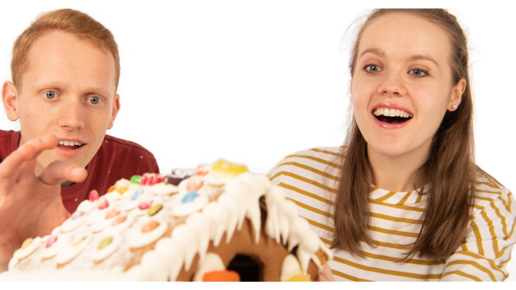 A man in a red t and a girl in a white and yellow striped one look amazed at a gingerbread house