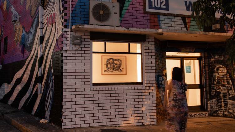 A woman on the street observes the art in the illuminated window gallery of Join the Dots artist-run collective