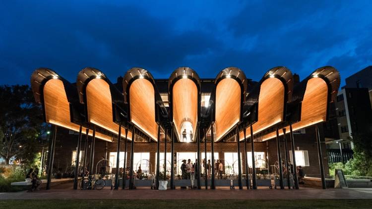 An exterior shot of the Joynton Avenue Creative Centre at dusk, with it's wooden arches aglow