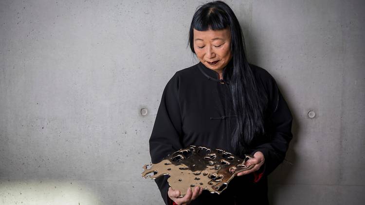 Artist Lindy Lee in black holding one of her gleaming flung bronze artworks