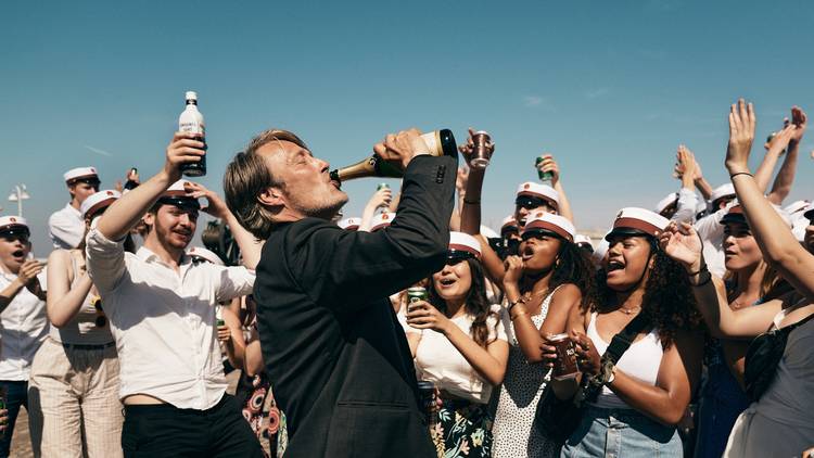 Mads Mikkelsen drinking a beer in front of high school graduates in sailor hats