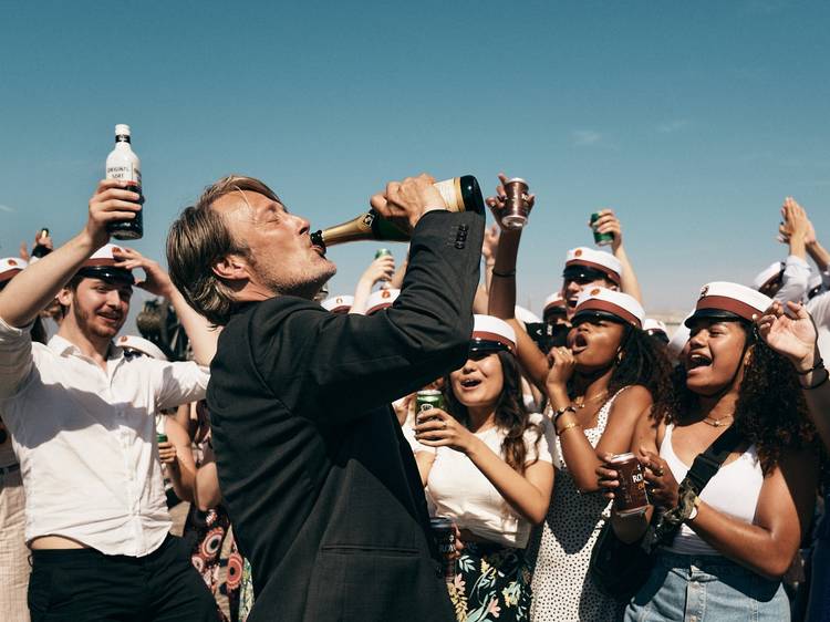 Mads Mikkelsen drinking a beer in front of high school graduates in sailor hats