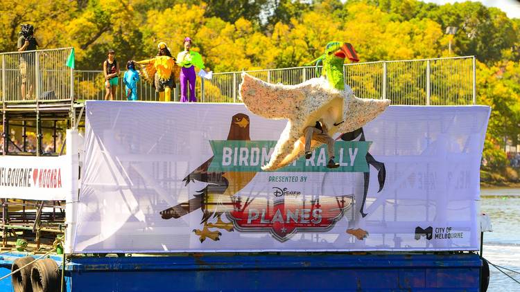 A person in a homemade bird costume jumps off a platform into the Yarra River