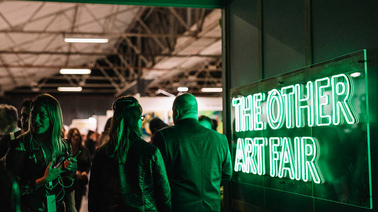 A green neon sign that says "THE OTHER ART FAIR" lights the entrance and faces of people at the Cutaway in Barangaroo.