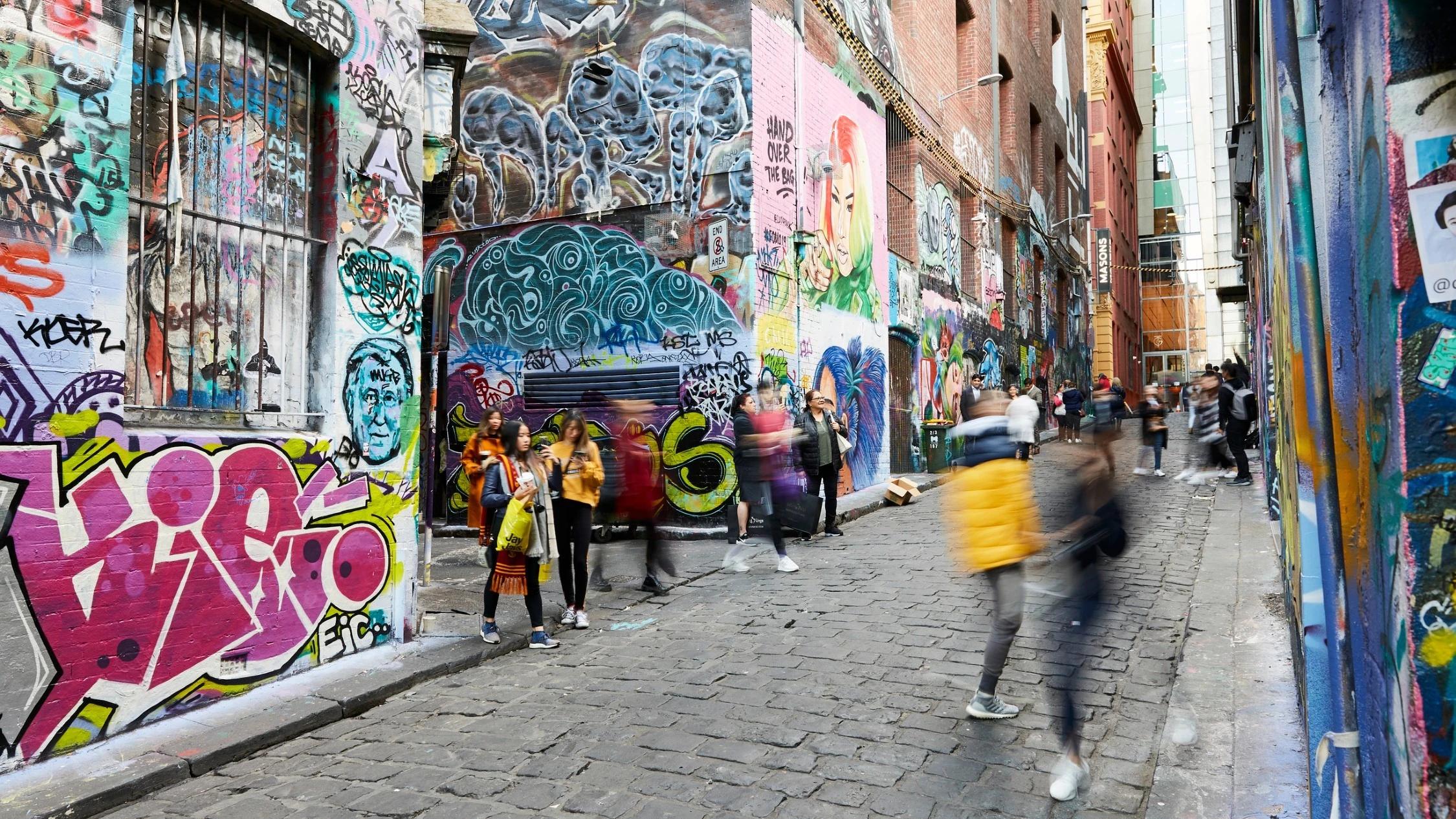 People walking through Hosier Lane which features bluestone pavers and street art all over the laneway