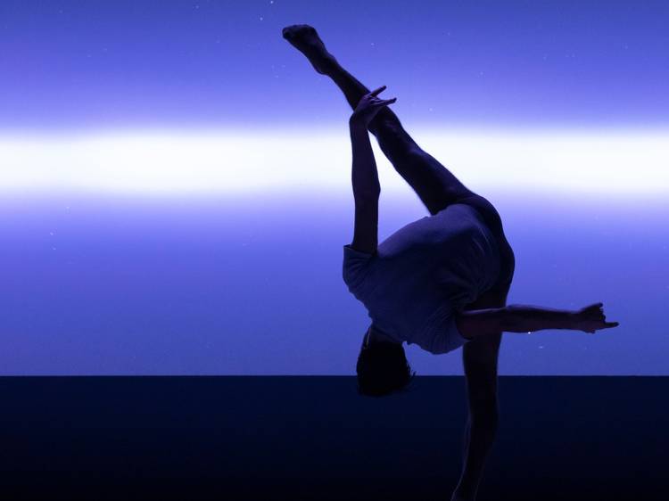 A dancer holds a leg aloft against a purple backdrop