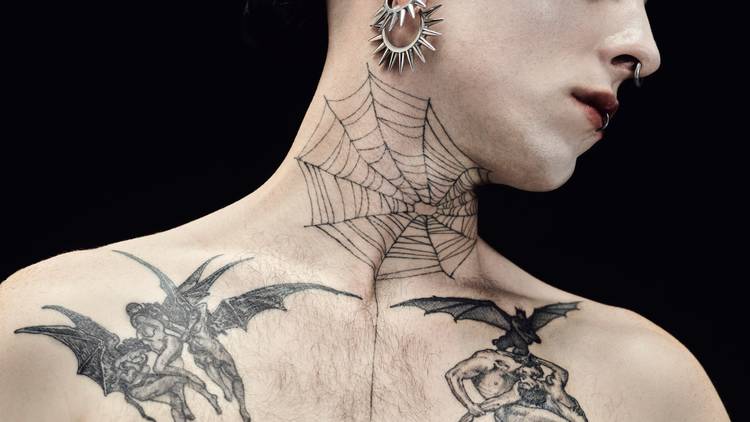 A close up of a pale man's lower face and upper torso with spider web tattoo