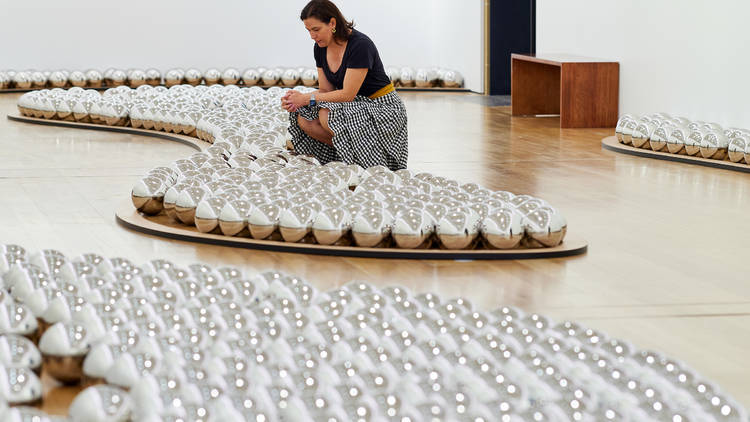 A person crouches by the reflective balls in the Narcissus Garden install at the Museum of Sydney
