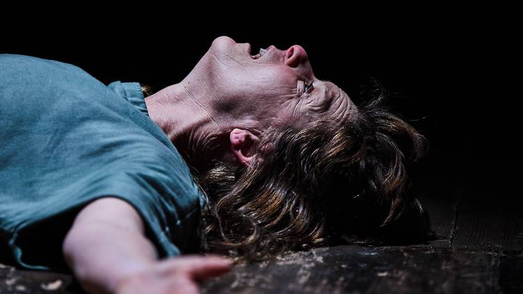 A close up of a woman, arms outstretched and gazing up exhausted at the ceiling