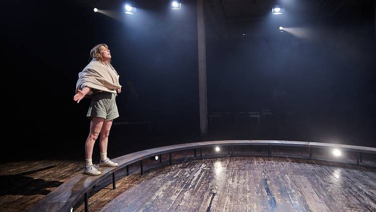 A woman standing on a ring platform, arms outstretched 