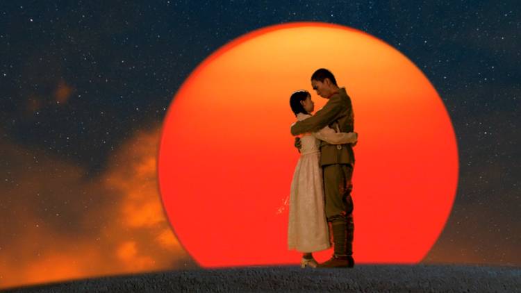 A man and woman embrace against a red sun 