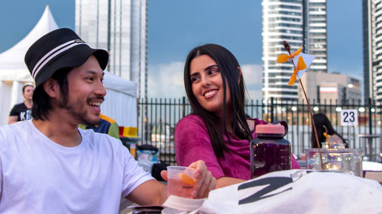 Two people enjoy drinks on a rooftop with Parramatta skyscrapers in the background
