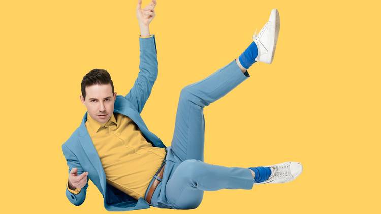 Nath Valvo legs akimbo in a pale blue suit against a yellow backdrop