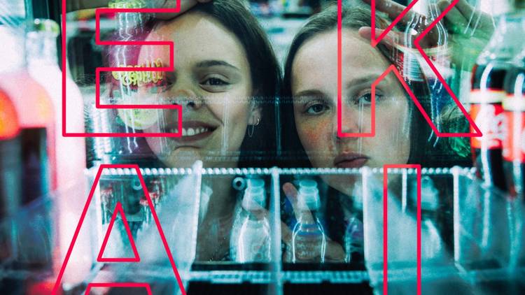 Two girls peer through the glass doors of soft drink fridge 