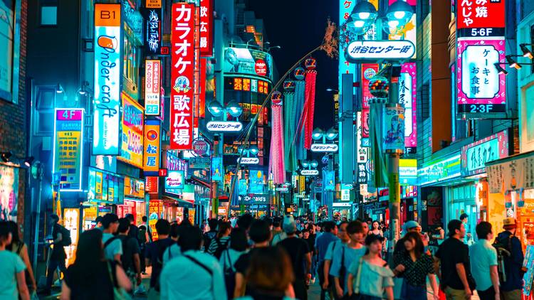 A crowd of people walking on a brightly lit street at night