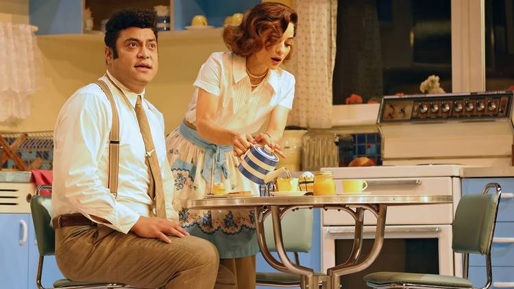 A man and a woman in 1950s attire sit at a diner-style table