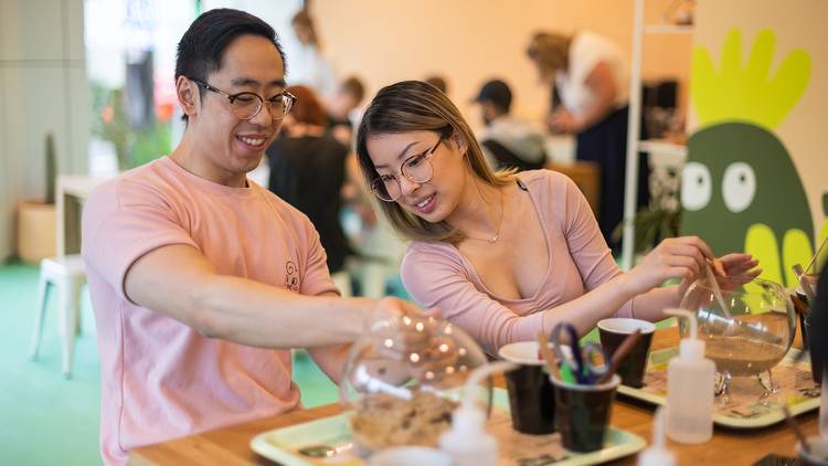 Two people sit at table, they are building terrariums.