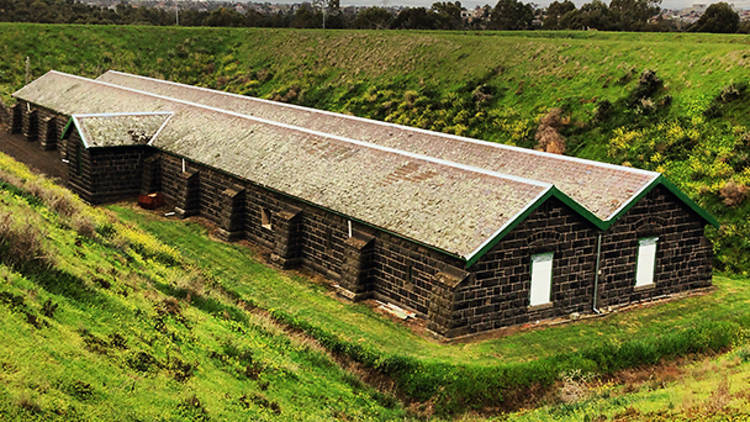 A long bluestone building located within a grassy ditch