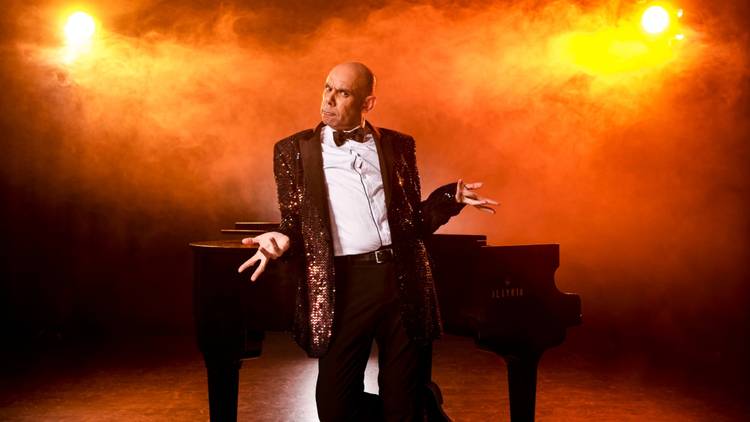 Cabaret star Steven Oliver in front of a piano, bathed in dramatic lighting