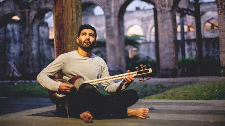 Hamed Sadeghi sitting cross-legged, playing the tar