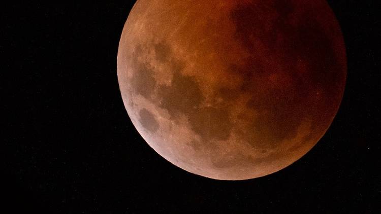 Close up of the Moon during lunar eclipse, the surface glows red and craters are visible.