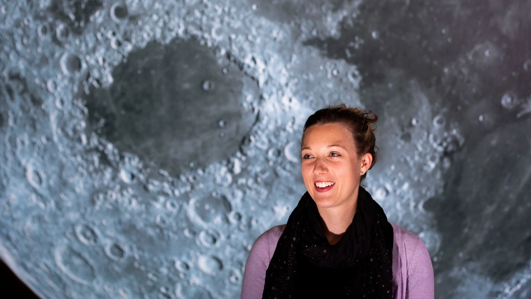 Dr Sarah Reeves smiles standing in front of large full moon.