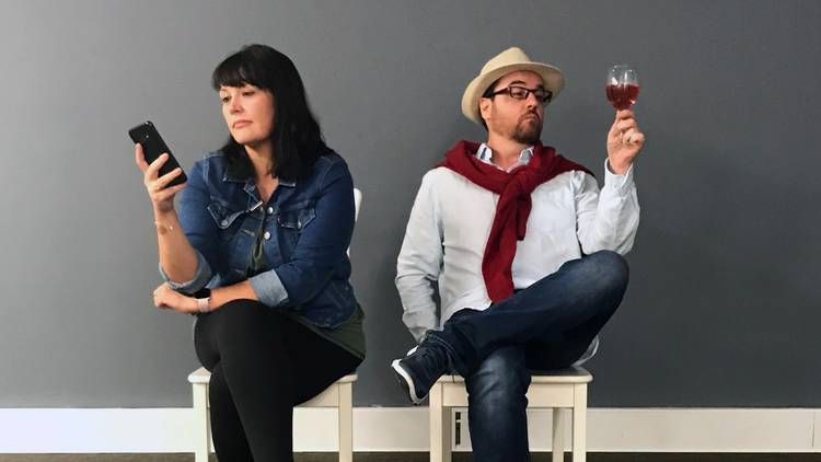 A woman on a phone and a man holding up a glass of red wine