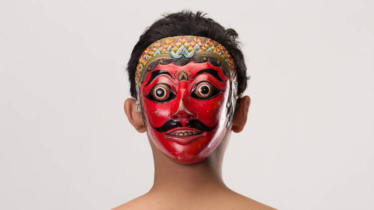 A photograph of a bright red Balinese mask worn on the back of someone's head