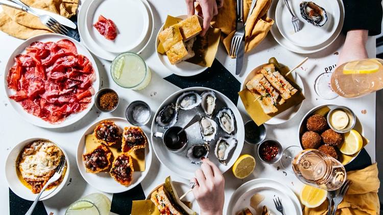 Table of food, hands reach for oysters and bread and assorted plates.