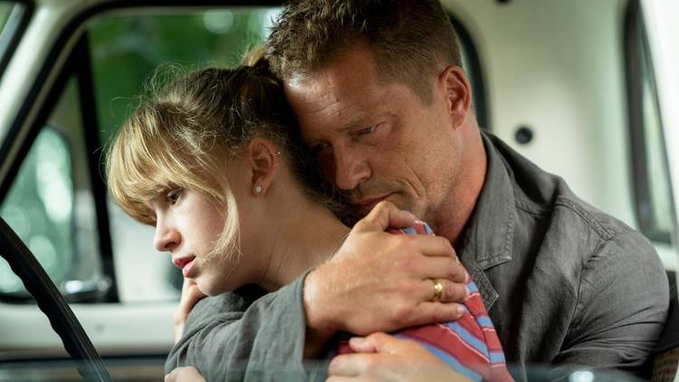 A dad hugs his teenage daughter in a car