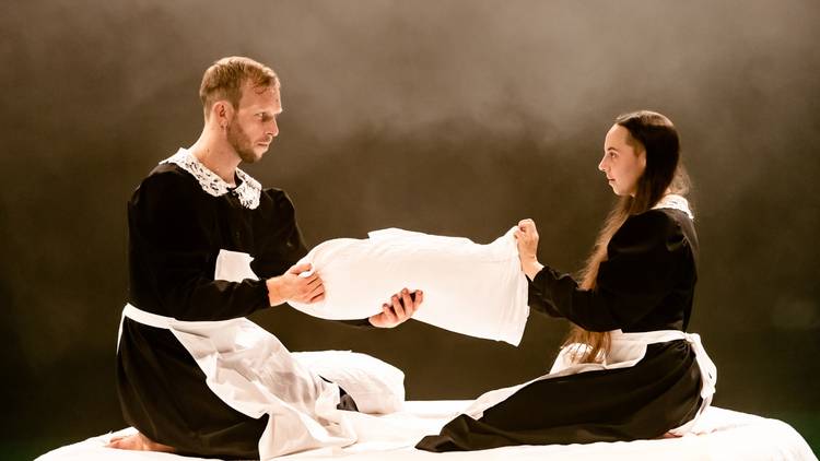 a man and a woman in maid outfits fold sheets