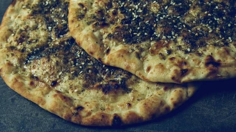 Two pieces of Zaatar, a Middle Eastern flatbread topped with oregano and seasame seeds.