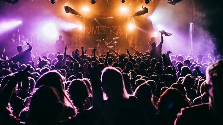 A view through a packed crowd with their hands in the air watching a band perform on the stage at the Metro.