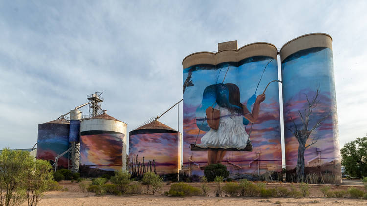 Large grain silos painted with a picture of a girl on a swing