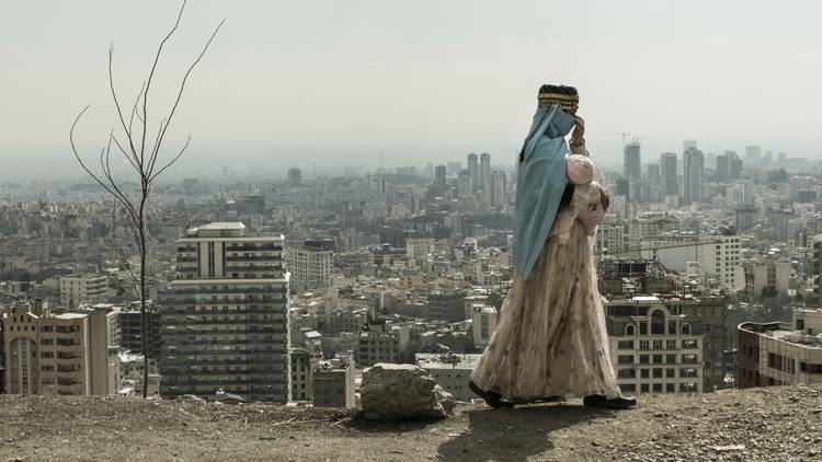 A woman walks in front of Tehran's skyline