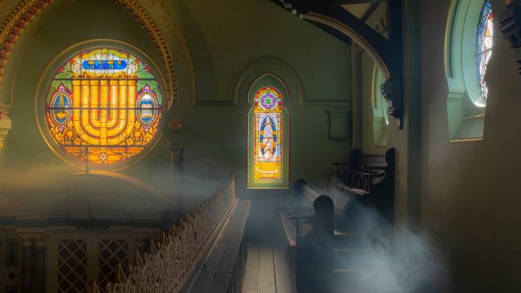 Stained glass windows cast coloured light through incense inside a synagogue