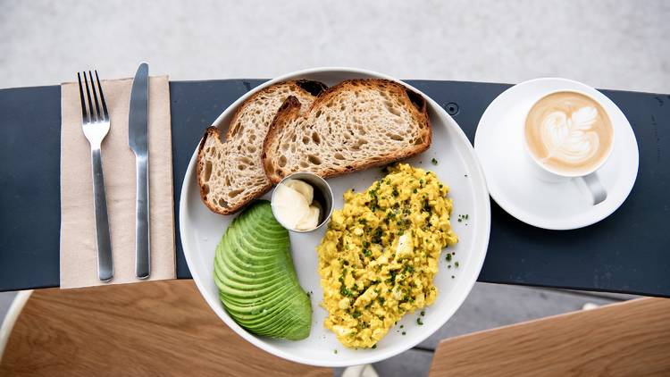 Eggs and toast on a bench with avocado on the side