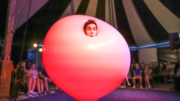 A man's face emerges from a giant pink bubble with an impressed audience in the background