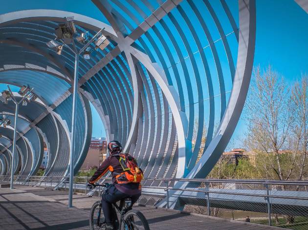 Madrid,/,Spain,-,03,17,2019:,People,Walk,Inside Madrid / Spain - 03 17 2019: People walk inside the Arganzuela modern metal footbridge outdoors at Madrid Rio green park across the Manzanares river downtown Madrid on a warm spring day.