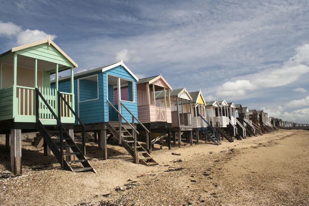 A row of colourful beach huts with small ladders descending onto a sandy beach at Thorpe Bay, Southend-on-Sea