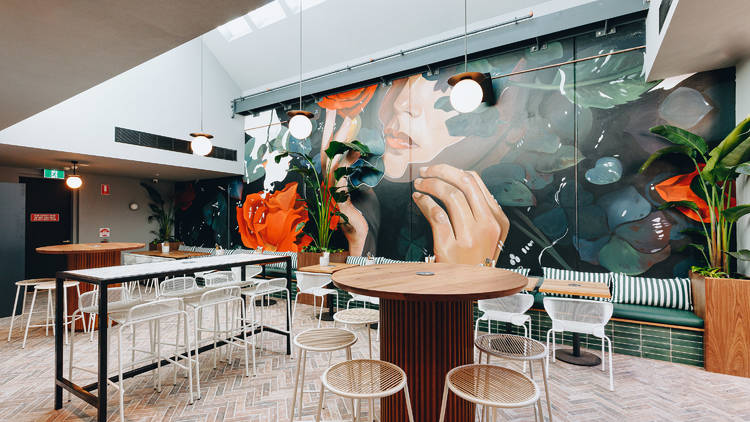 A view of the outdoor terrace with parquetry brick flooring, a whole-wall mural of a person emerging from a bush and clean, sleek outdoor furniture.