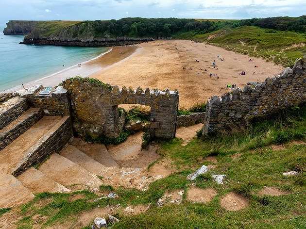 Barafundle Bay in Wales A shot of stone steps descending through a ruined stone archway to the yellow sand of Barafundle Bay, with the blue ocean on the left and grassy banks to the right of the beach