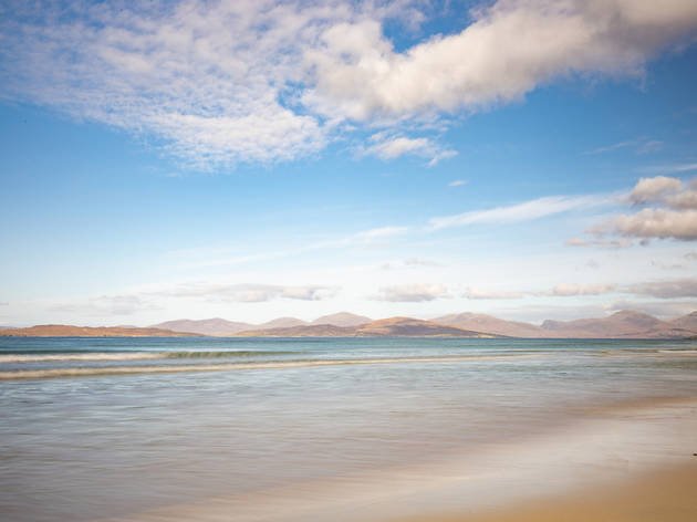 Long,Exposure,On,Scarista,Beach,,Isle,Of,Harris Long exposure shot of Scarista beach, with yellow sand in the foreground, blurry water stretching into the distance, faded mountains in the background and a blue cloudy sky overhead