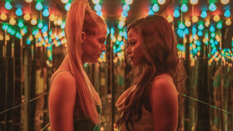 Two women stare at each other bathed by neon light